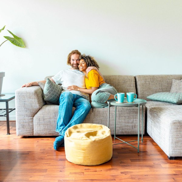 Cheerful multiracial couple sitting on sofa in the living room – Happy family moving in new home – Real estate and stylish furniture concept Cheerful multiracial couple sitting on sofa in the living room - Happy family moving in new home - Real estate and stylish furniture concept
